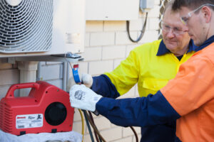 Two men working on an aircon unit outside | Featured image for Why Become an Electrician blog.