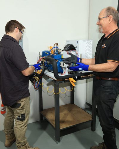 Men smiling while working on refrigeration unit | Two men working on refrigeration unit | Featured image for Certificate III in Refrigeration & Air Conditioning on Get Skilled Training