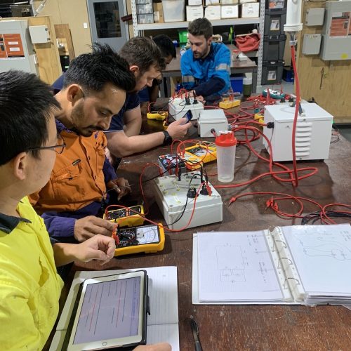 Five men at a bench working on electrical equipment