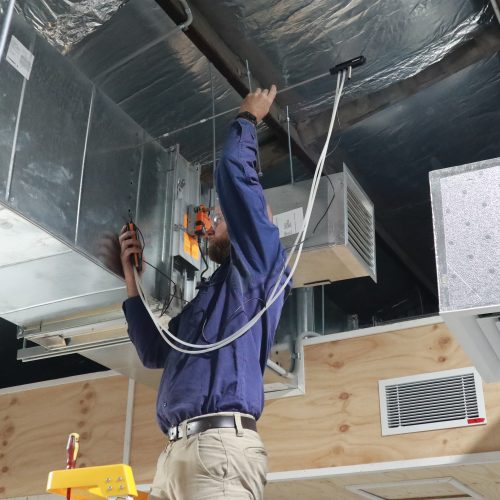 Man standing on a ladder working on air vents.