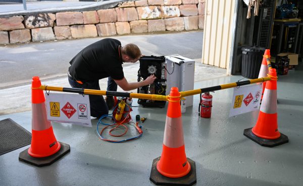 Man installing gas fittings behind safety barrier | Featured image for Gas Work License Hydrocarbon page on Get Skilled Training.