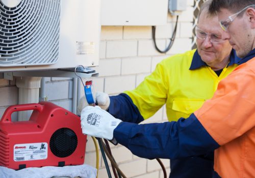 Two men working on an aircon unit outside | Featured image for Why Become an Electrician blog.